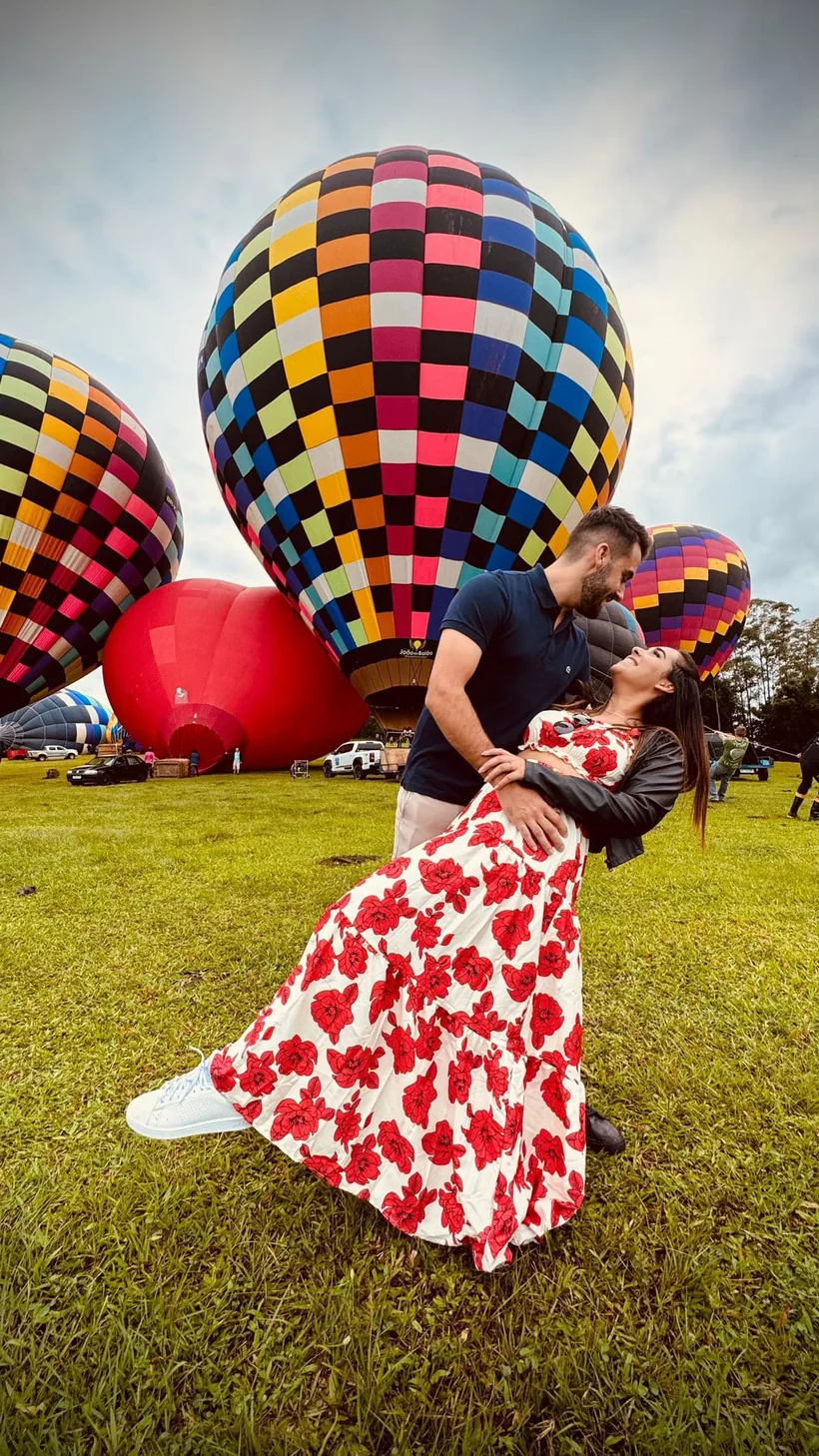 Casal dançando em frente aos balões coloridos no campo ao amanhecer