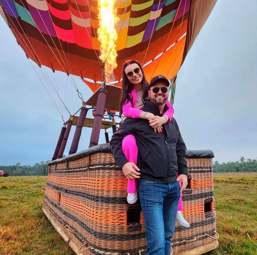 Casal abraçado no cesto de um balão do João do Balão, com o maçarico aceso ao fundo